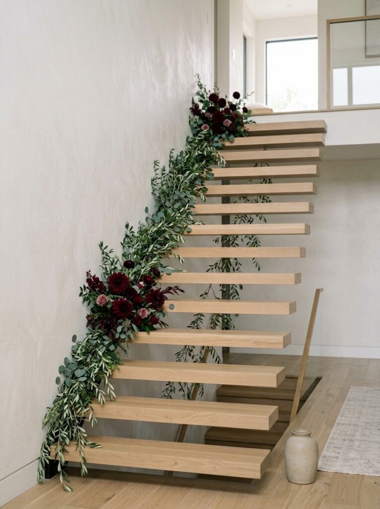 Asymmetrical olive branch and dark dahlia garland on a modern floating staircase.